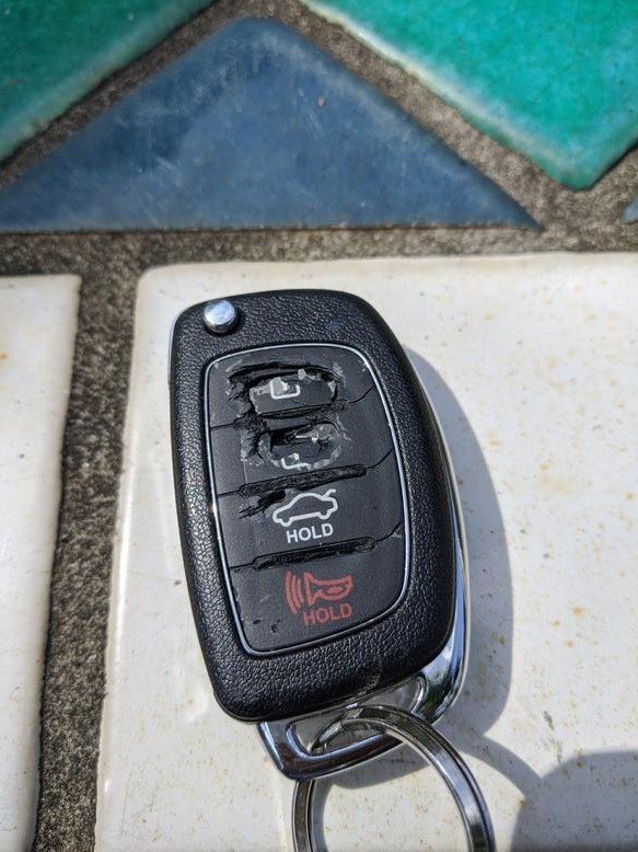 Close-up of a severely cracked and disintegrated Hyundai key fob case, showing worn-out button area.