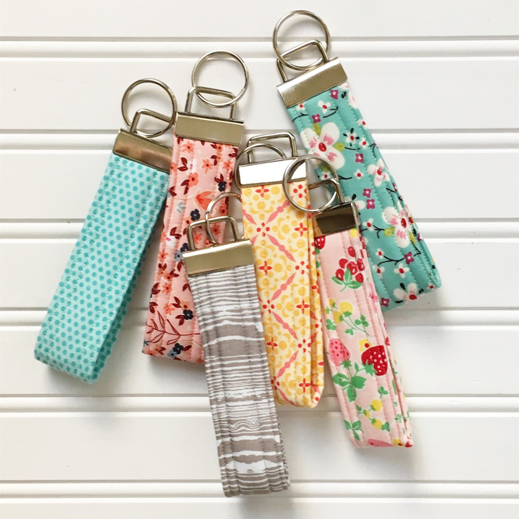 Key fobs displayed on a wooden surface, showcasing various fabric patterns and hardware.