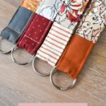 Close-up shot of colorful handmade key fobs showcasing various fabric patterns, alongside sewing supplies like fabric scraps, key rings, and thread, perfect for DIY crafting enthusiasts.